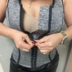 Faja chaleco reductora unisex gris con cremallera y broches, mujer ajustando.