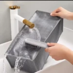 Organizador gris de ropa interior de tela con cepillo y agua bajo grifo dorado.