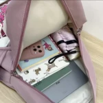 Interior de morral lila abierto mostrando un celular con funda rosa, cuadernos y un iPad gris, bien organizado.