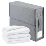 Caja organizadora gris con asas para ropa de cama, apilada sobre otra, con sábanas blancas dobladas al frente.
