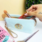 Cosmetiquera azul claro escarchada con brochas y labial en su interior, detalle ovalado dorado.