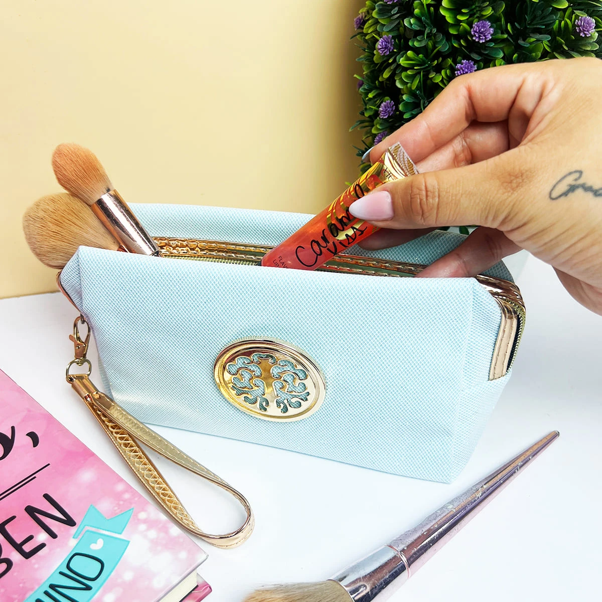 Cosmetiquera azul claro escarchada con brochas y labial en su interior, detalle ovalado dorado.