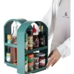 Organizador giratorio de especias y aceites, dos niveles, color verde azulado, usado en cocina por persona con delantal.