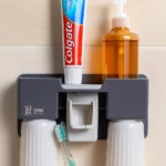 Organizador de baño gris con dispensador de jabón, pasta de dientes Colgate y cepillos dentales en vasos blancos.