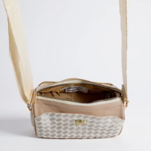 Bolso cruzado pequeño Karla Chacon, color beige, abierto mostrando forro interior y placa con logo sobre textura tejida inferior.