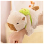 Pulsera peluche capibara beige con mochila verde, accesorio suave para muñeca.