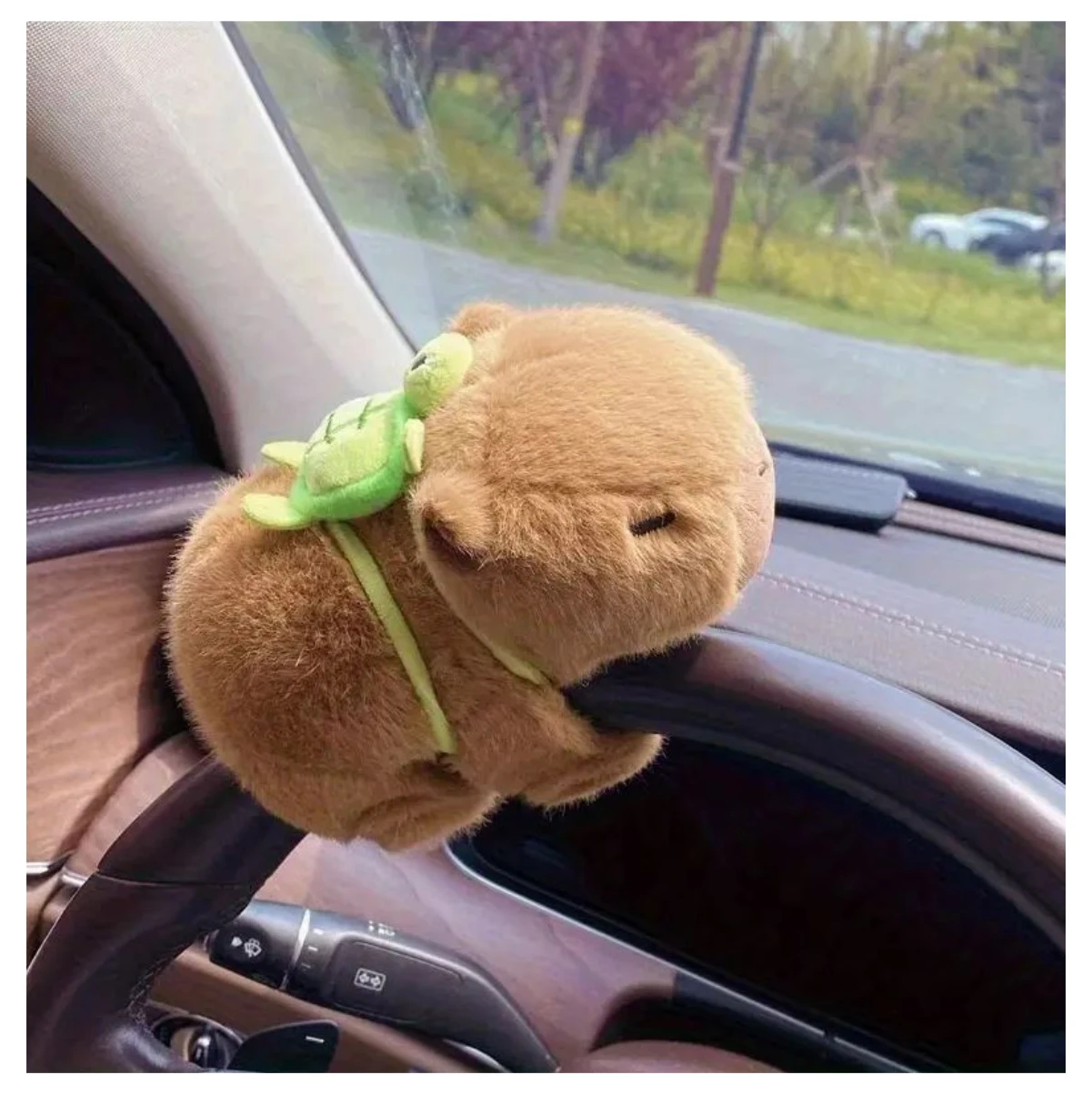 Peluche de capibara marrón con tortuga verde en la espalda, sujetado al volante de un auto.
