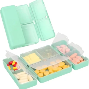 Pastillero magnético verde menta con 7 compartimentos, abierto y mostrando diferentes píldoras y cápsulas.