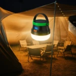 Lámpara solar exterior led bombillo 50W, portátil, con pantalla digital, iluminando un campamento con mesas y sillas bajo una carpa.