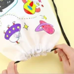 Mochila mágica blanca con diseño espacial para colorear, fondo amarillo, cierre de cordón.