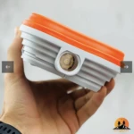 Lámpara solar LED 150W, portátil, diseño plegable blanco y naranja, con linterna frontal.