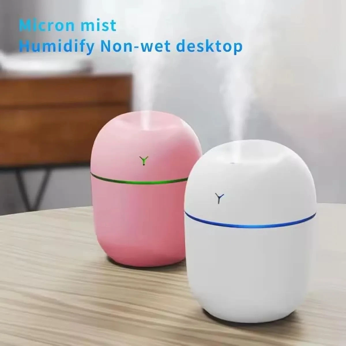 Dos humidificadores ultrasónicos mini, uno rosa y otro blanco, emiten vapor sobre un escritorio.