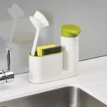 Dispensador de jabón blanco con tapa verde y organizador para cepillo y esponja de cocina.