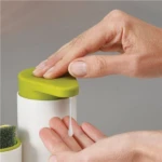 Dispensador de jabón blanco con tapa verde dispensando líquido sobre mano.