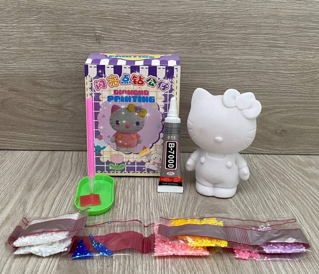 Set de pintura de diamante Hello Kitty blanca, caja morada, pegamento B-7000, aplicador y bolsitas con diamantes de colores.