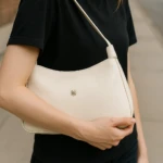 Bolso praga beige de dama Karla Chacón, textura piel, color crema, colgado al hombro.