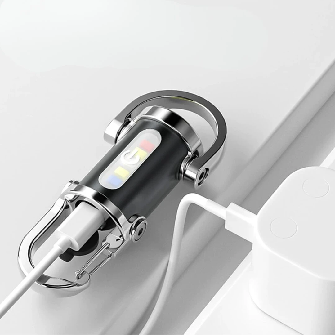 Linterna llavero negra y cromada cargando vía cable USB-C, con indicador de encendido y luces de colores.