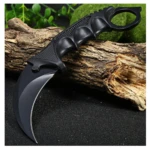 Cuchillo Karambit negro táctico con mango de anillo, hoja curva, sobre tronco y fondo oscuro con brillo.