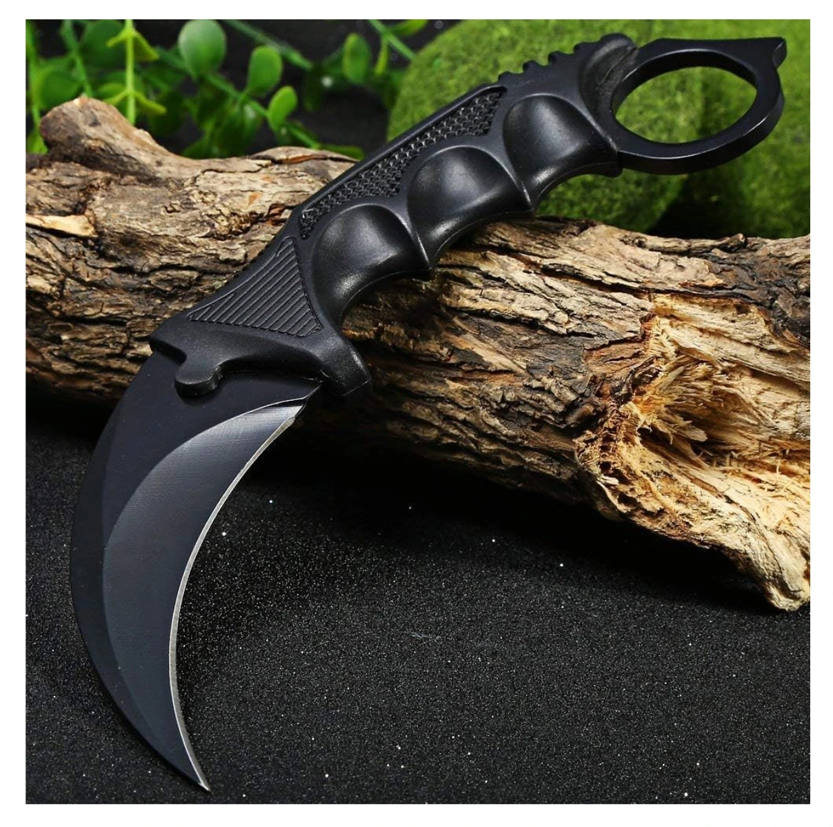 Cuchillo Karambit negro táctico con mango de anillo, hoja curva, sobre tronco y fondo oscuro con brillo.