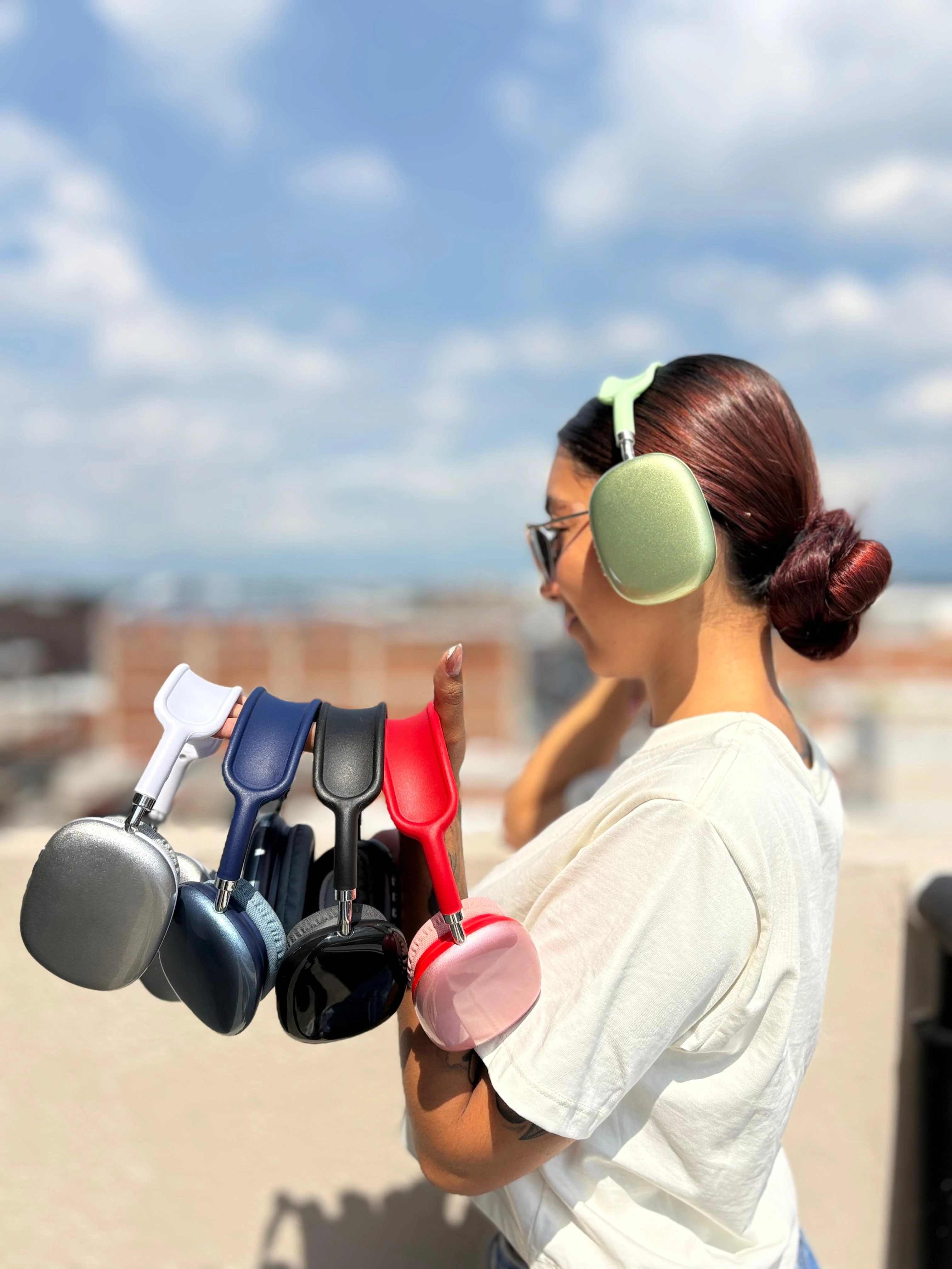 Mujer morena con cabello recogido y gafas sostiene varias Diademas P9 de colores: verde lima puesta, plata, azul oscuro, negro, rojo y rosa.