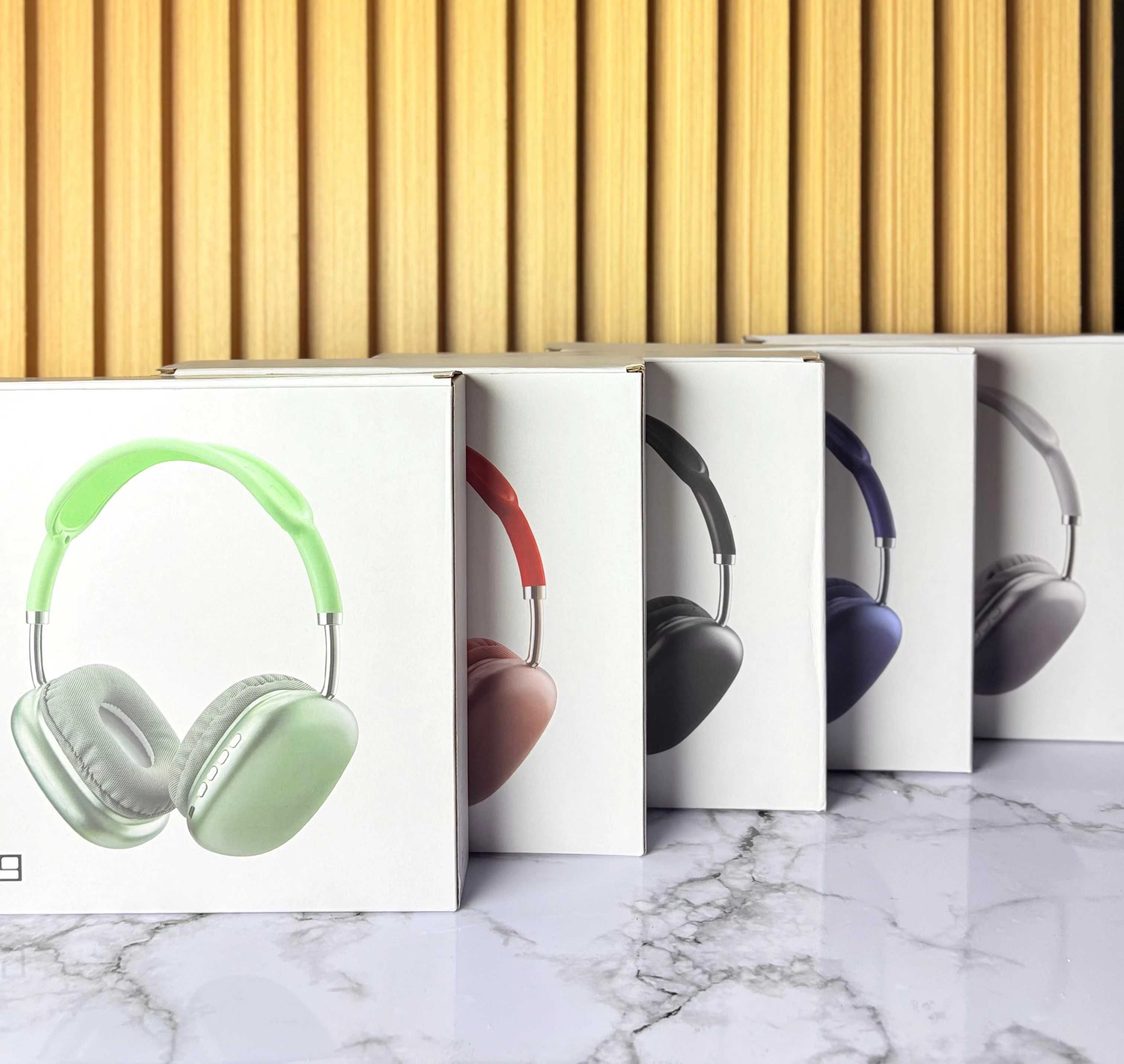 Diadema P9 en empaques blancos, mostrando versiones verde claro, roja, negra, azul y gris, sobre superficie de mármol y fondo de listones de madera.