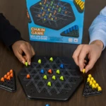 Juego de mesa Chain Game, tablero hexagonal negro con piezas de colores, manos colocan fichas.