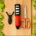 Afilador de cuchillo naranja y negro, tijeras y pelador negro sobre tabla de cortar de madera con lechuga.