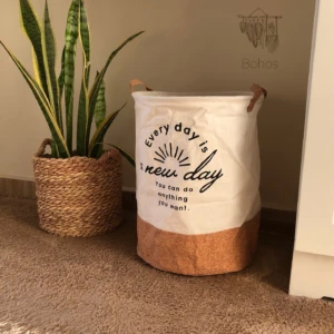 Cesto organizador blanco y corcho con texto inspirador junto a planta Sansevieria en maceta de fibra natural.
