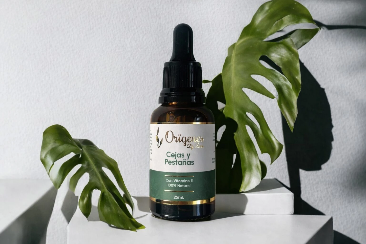 Serum Origenes para cejas y pestañas, frasco de vidrio ámbar con gotero, hojas verdes de monstera.