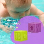 Bloques de silicona para bebés en forma de cubo, uno verde con figuras de flor y otro morado con pentágono, flotando en agua.