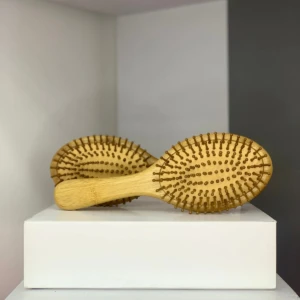 Dos cepillos de pelo ovalados con base y cerdas de bambú natural, uno detrás del otro, sobre una caja blanca.