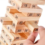 Jenga de madera natural, mano retirando bloque numerado 26 en torre inestable.