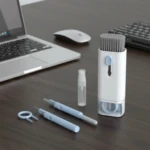 Kit de limpieza para computadora con cepillo retráctil blanco, herramientas azules para teclas y atomizador, junto a laptop y mouse.