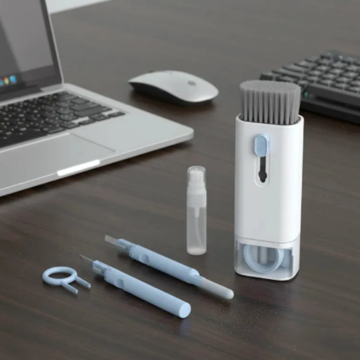 Kit de limpieza para computadora con cepillo retráctil blanco, herramientas azules para teclas y atomizador, junto a laptop y mouse.