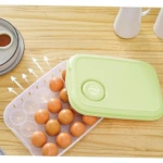 Organizador de huevos transparente para 20 unidades con tapa verde claro, sobre mesa de madera.