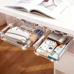 Dos cajones organizadores transparentes debajo de un escritorio blanco, llenos de suministros de oficina como grapadoras, notas y calculadora.