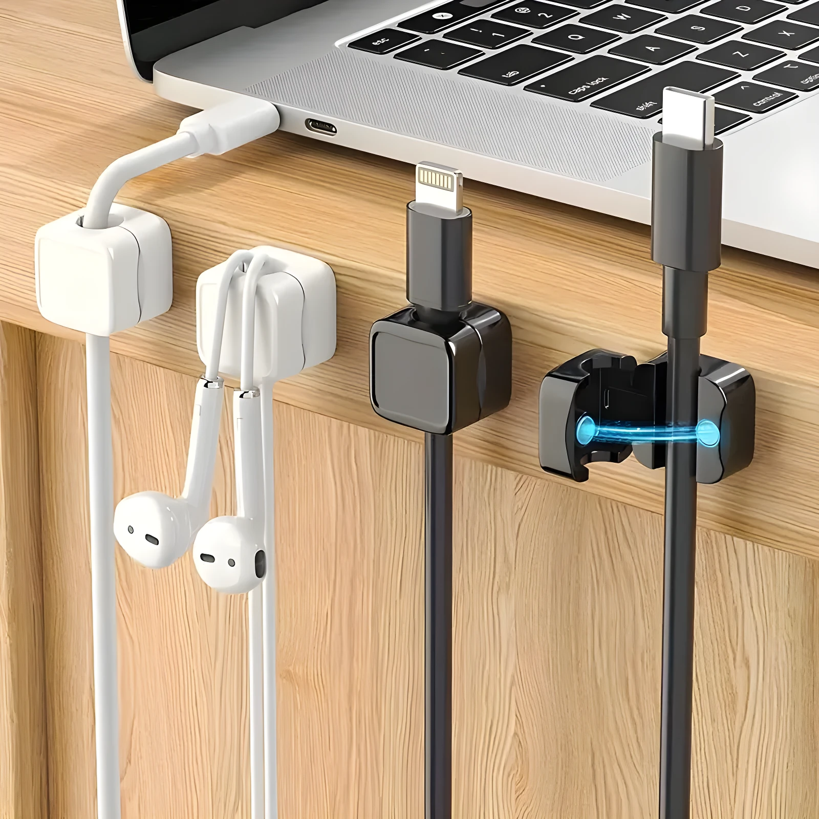 Organizador magnético de cables en colores blanco y negro, instalado en el borde de un escritorio de madera, sosteniendo auriculares y cables USB.
