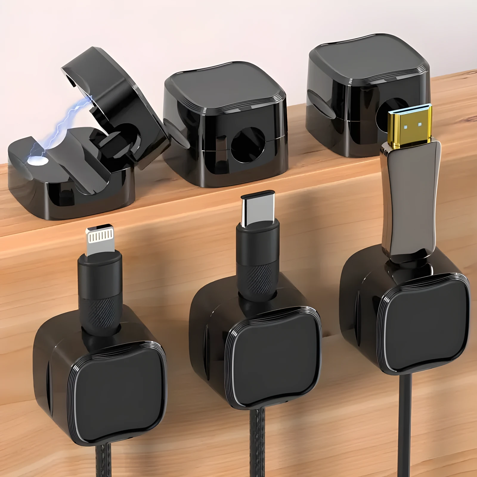 Cinco organizadores de cables magnéticos negros sobre madera, tres con conectores tipo Lightning, USB-C y HDMI insertados, y dos cubos libres superiores.
