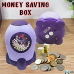 Alcancía infantil morada con diseño de cohete, ventana transparente con esferas, y monedas esparcidas.