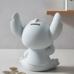 Alcancía blanca de Stitch sentado con los brazos levantados, listo para pintar, con monedas al frente.