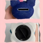 Alcancía azul con forma de oso, decorada con diamantes y un moño rosa. Vista inferior muestra tapa blanca con ranura para monedas.