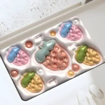 Tapete de baño con relieve 3D de fresas coloridas, textura brillante y base antideslizante, junto a zapatillas blancas.