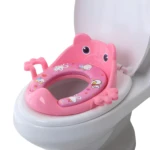 Asiento entrenador de inodoro rosado con diseño de animal y bordes acolchados con dibujos animados, puesto sobre taza de baño blanca.