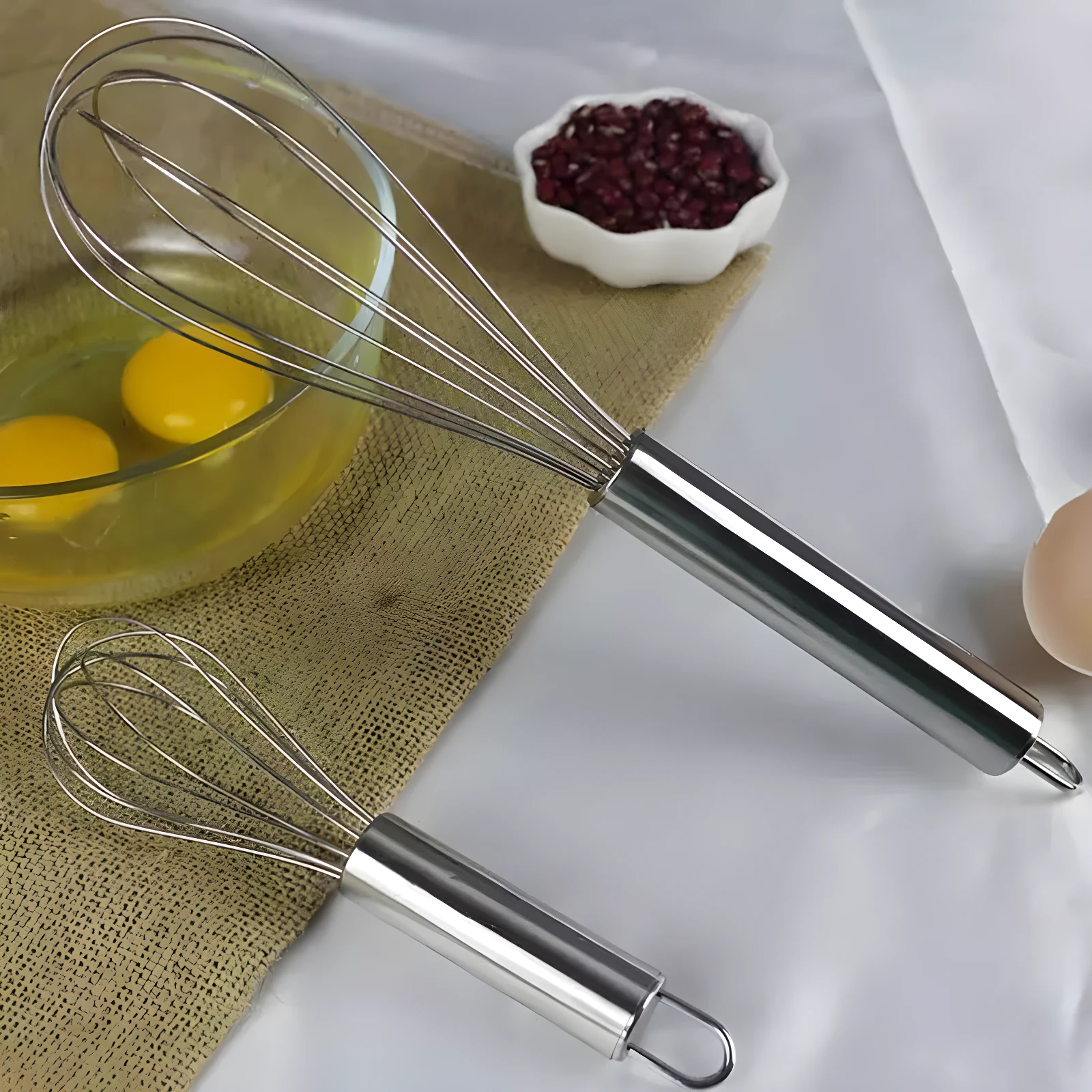 Set x3 batidores manuales acero inoxidable con huevos y frijoles rojos en cuenco.