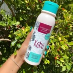 Biomascarilla Capilar Kaba Hidratación Profunda 500 ml, en mano frente a follaje verde y frutos rojos.