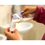 Manos vertiendo leche materna desde bolsa de almacenamiento a vaso dosificador marcado en onzas y cc.
