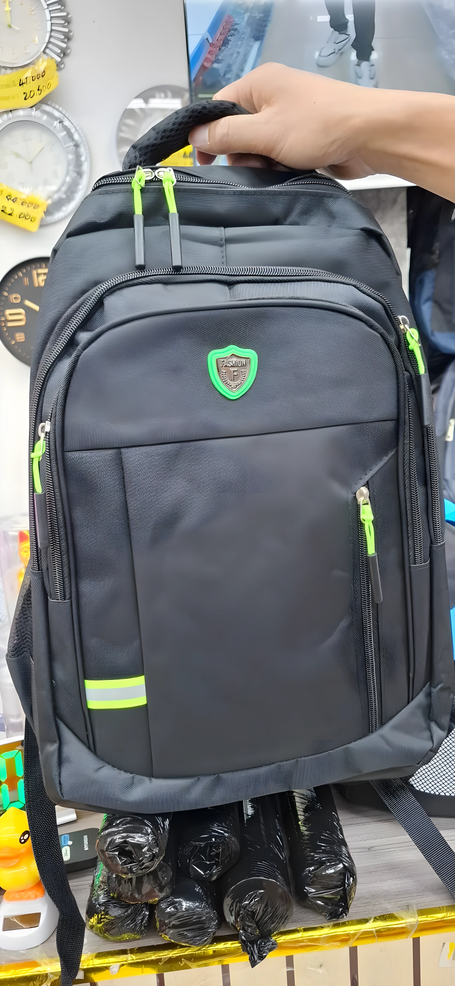 Mochila negra con detalles fluorescentes, logo verde y cierre frontal.