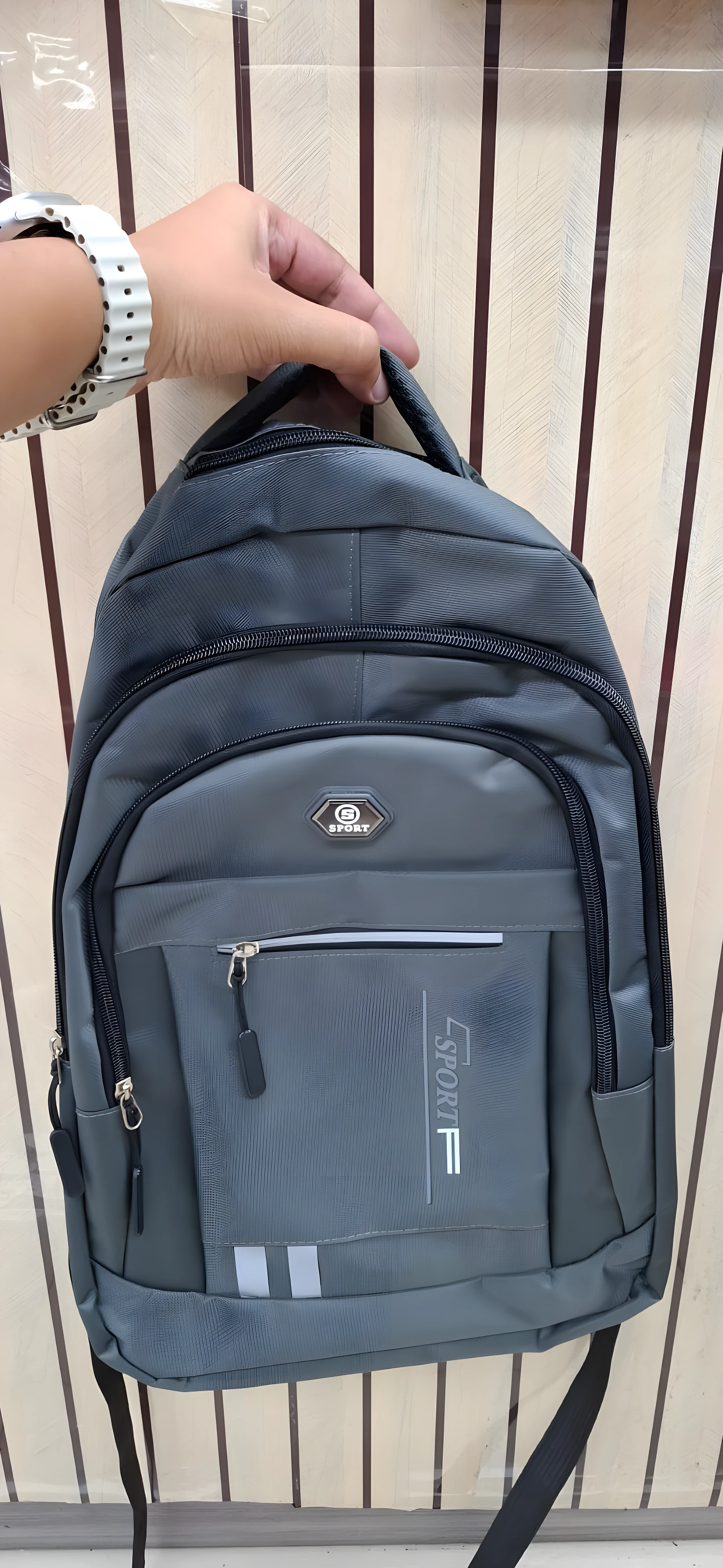 Mochila gris deportiva de viaje o escolar para dama y caballero, con logo "SPORT" y detalles reflectantes.