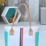 Bolso playero blanco con detalles en turquesa, rayas verticales rojas y azul marino. Incluye etiqueta "NEW YORK".