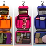 Tres bolsos organizadores viajeros colgantes abiertos: naranja con artículos de aseo, fucsia con gafas de sol y azul con ropa doblada.